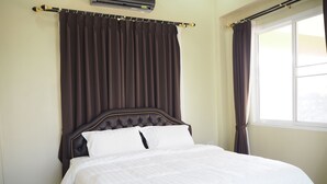 A neatly made bed with a dark headboard and white bedding, a window with curtains, and patterned floor tiles. - Baan Tukta (Cha-am)