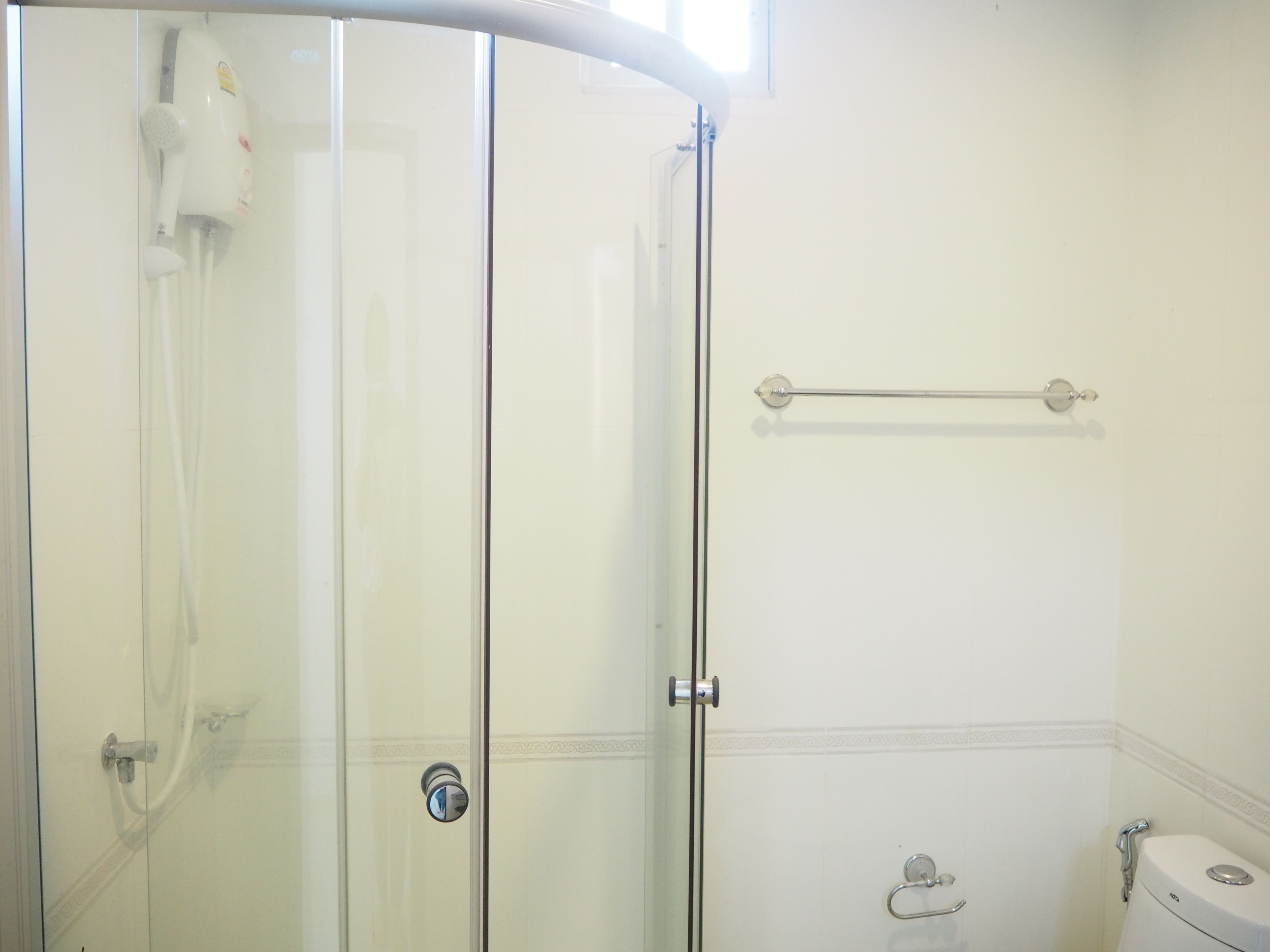 A glass-enclosed shower with a handheld showerhead, a towel rack, and a toilet.