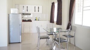 A modern kitchen with white cabinets, a stainless steel refrigerator, and a glass dining table with four chairs. - Baan Tukta (Cha-am)