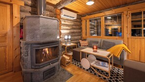Interior acogedor de una cabaña de troncos con chimenea de piedra, paredes de madera y un sofá con una manta amarilla.