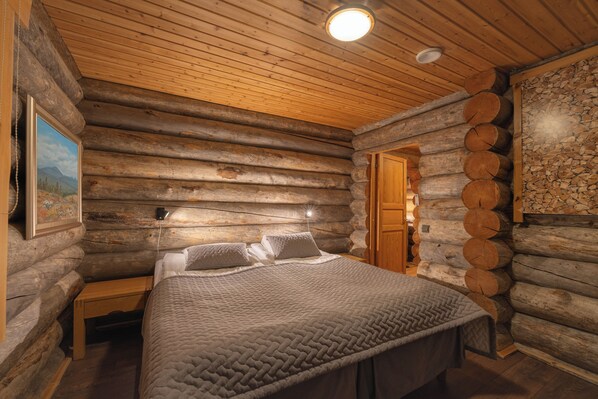 Un dormitorio de cabaña de troncos con cama, paredes de madera, un cuadro y una pared de piedra.