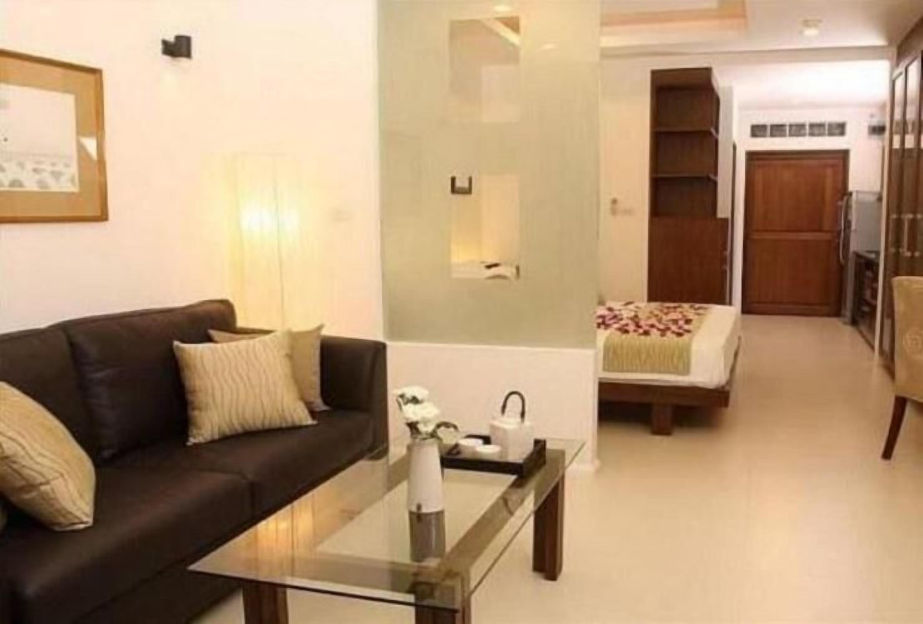A modern living room with a glass coffee table, a dark brown sofa, and a bed with a floral bedspread.