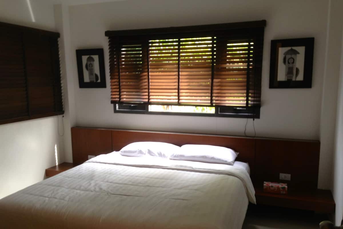 A bedroom with a large bed, wooden headboard, and a window with blinds.