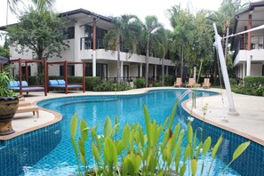Una piscina rodeada de sillas de descanso y un edificio con balcones.