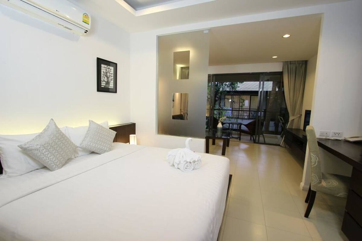 A hotel room with a large bed, a desk, and a view of the outdoor area.