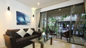 A modern living room with a glass coffee table, a dark leather sofa, and a large window offering a view of the outdoors. - TSE Residence by Samui Emerald Condominiums (Koh Samui)