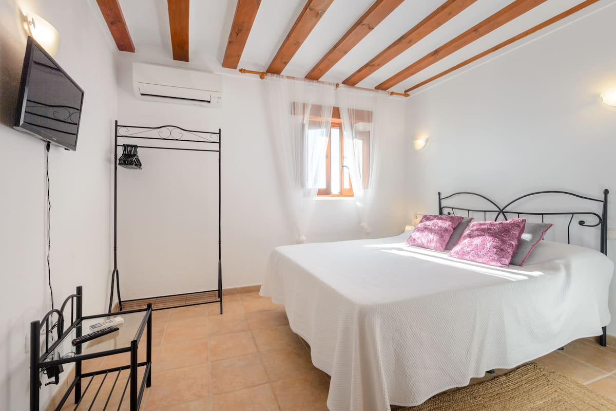 A bedroom with a bed, a TV, an air conditioner, a window with curtains, and a door.