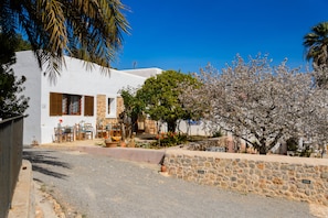 A white building with a stone wall and a garden with flowering trees. - Agroturismo Can Prats (Santa Eulalia del Rio)