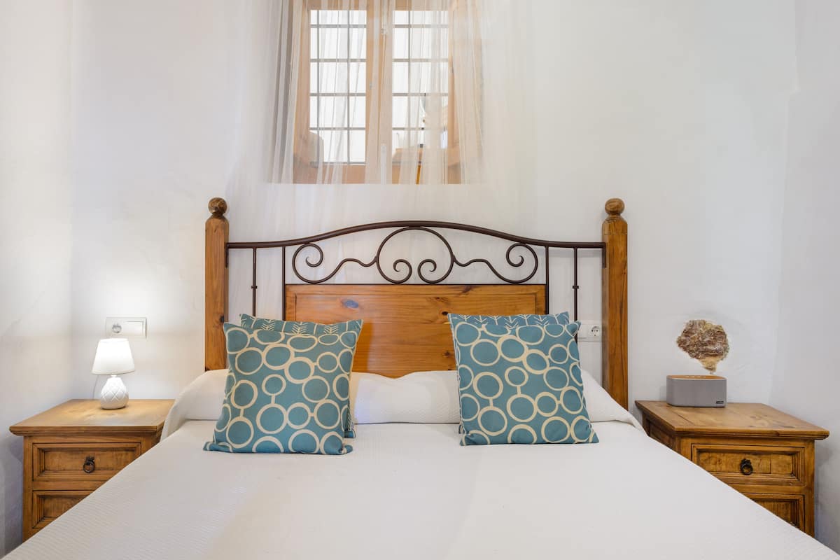 A neatly made bed with two patterned pillows, a bedside lamp, and a small decorative item on a wooden nightstand.