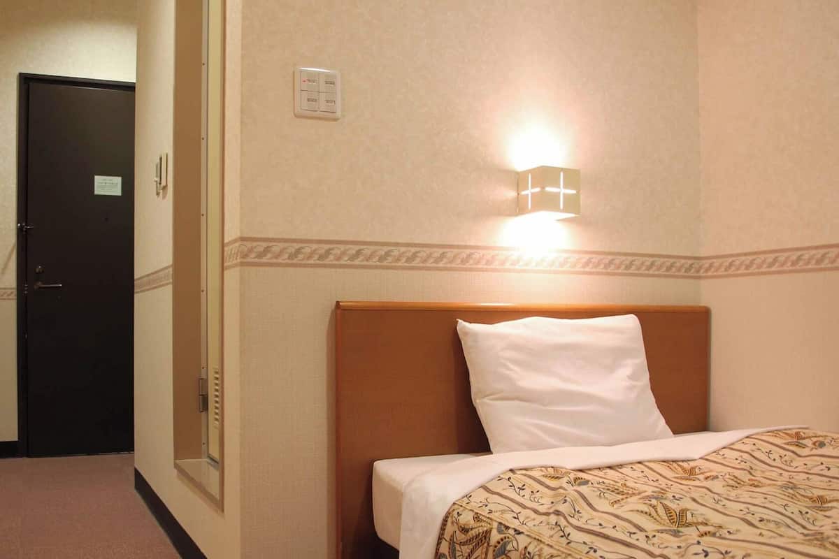 A hotel room with a bed, a nightstand, a wall-mounted light, and a door.