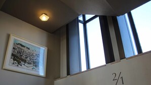 Uma escadaria com corrimão de metal, um quadro emoldurado de um edifício e uma janela com vista para o céu.