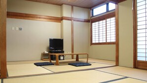 Quarto japonês tradicional com tatames, uma televisão e uma pequena mesa.