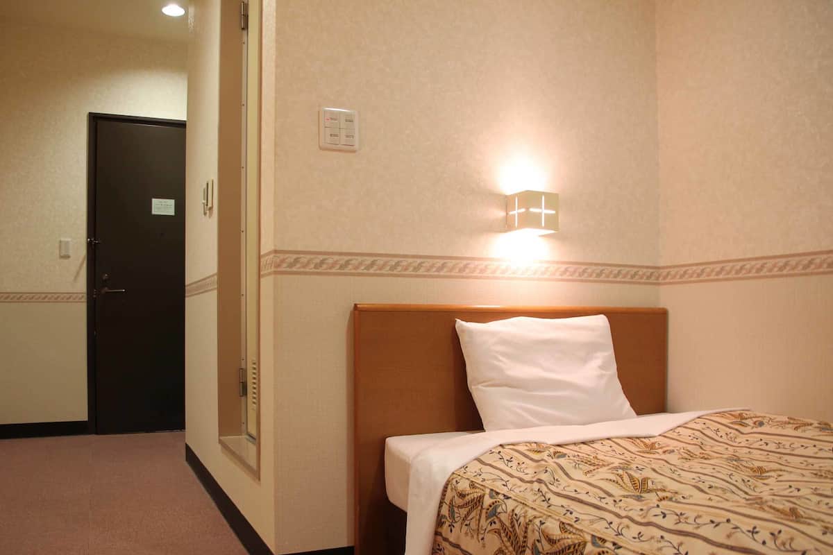 A hotel room with a bed, a nightstand, a wall-mounted light, and a door.