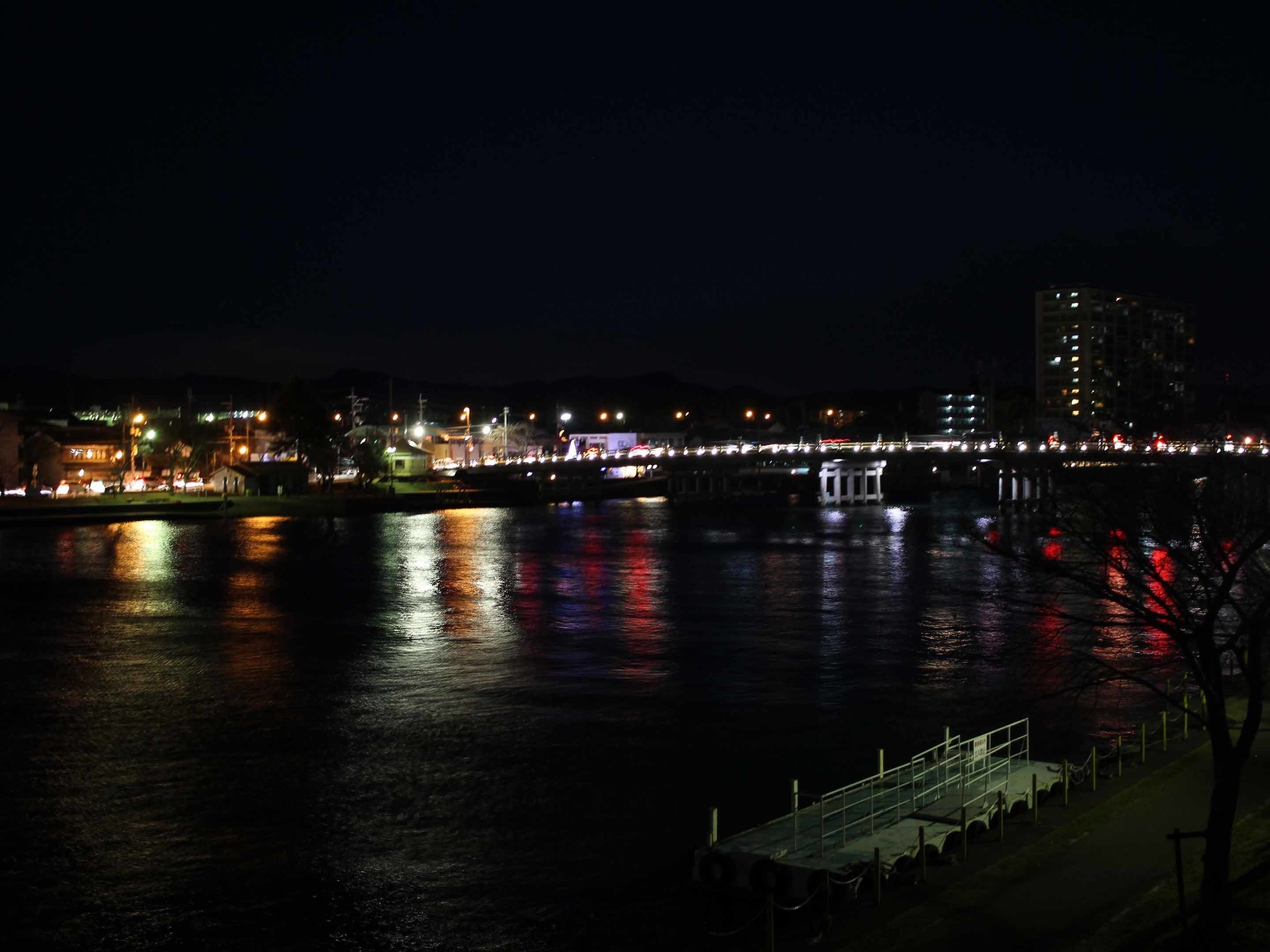A nighttime view of a waterfront area with a bridge, buildings, and a dock.