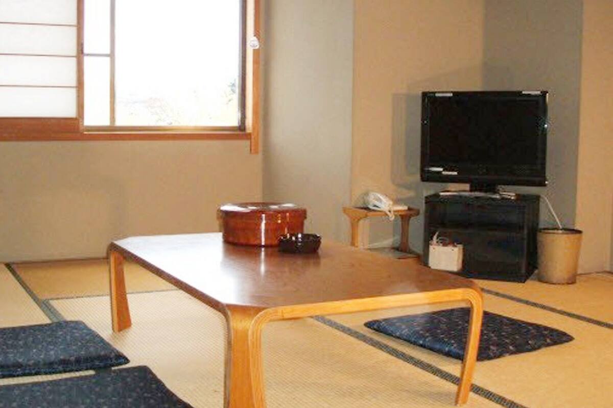 A tatami mat room with a low table, cushions, a television, and a small cabinet.