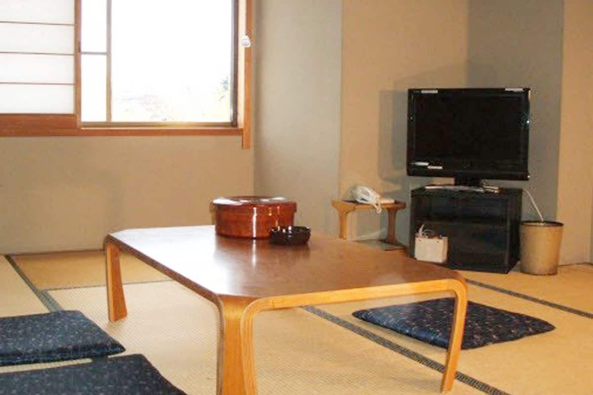 A tatami mat room with a low table, cushions, a television, and a small cabinet.