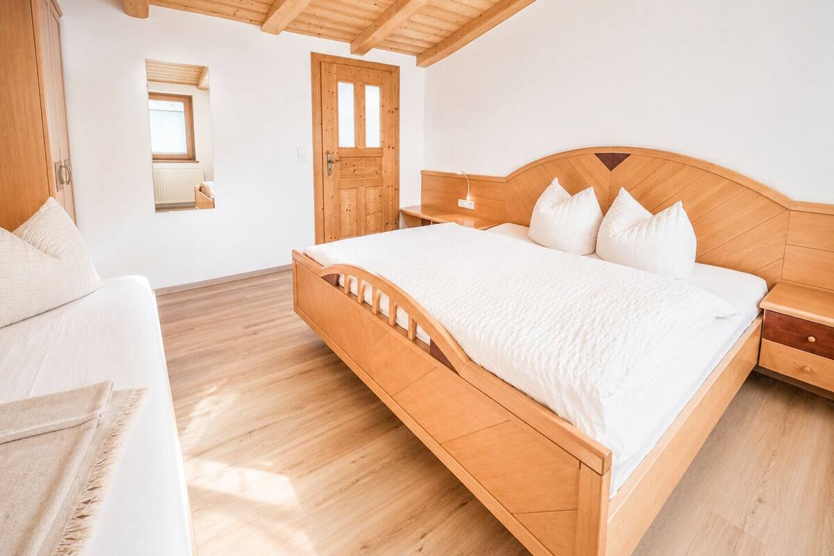A bedroom with a wooden bed, a bedside table, a nightstand, a window, and a door.