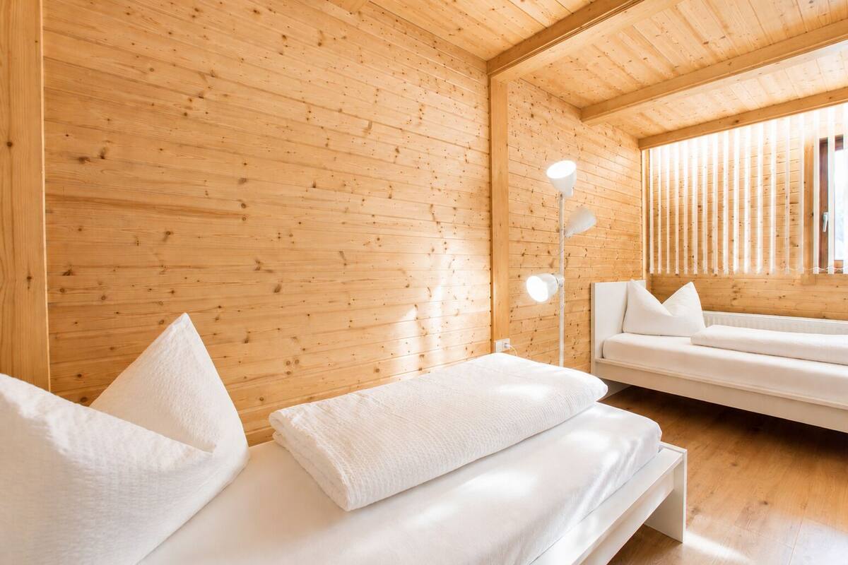 A wooden cabin interior with a bed, a sofa, and a floor lamp.