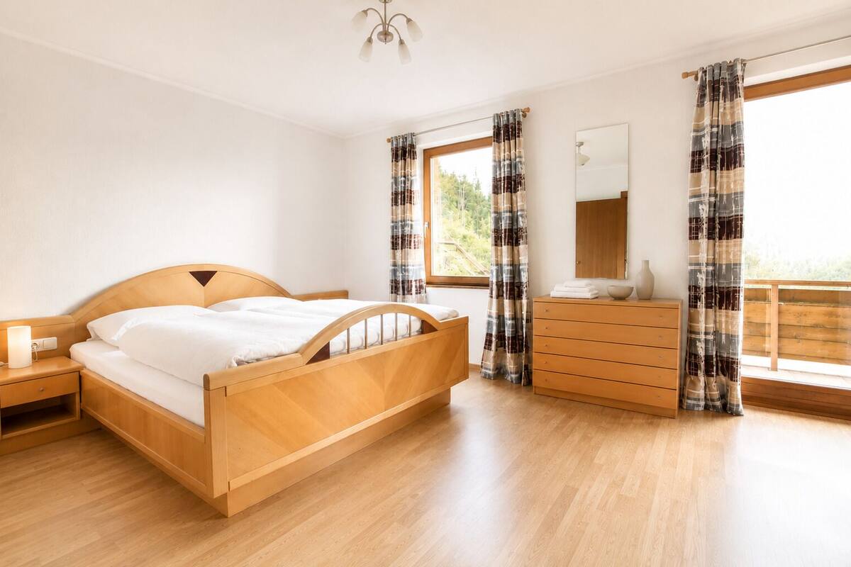 A bedroom with a wooden bed, a nightstand, a dresser, and a window with curtains.