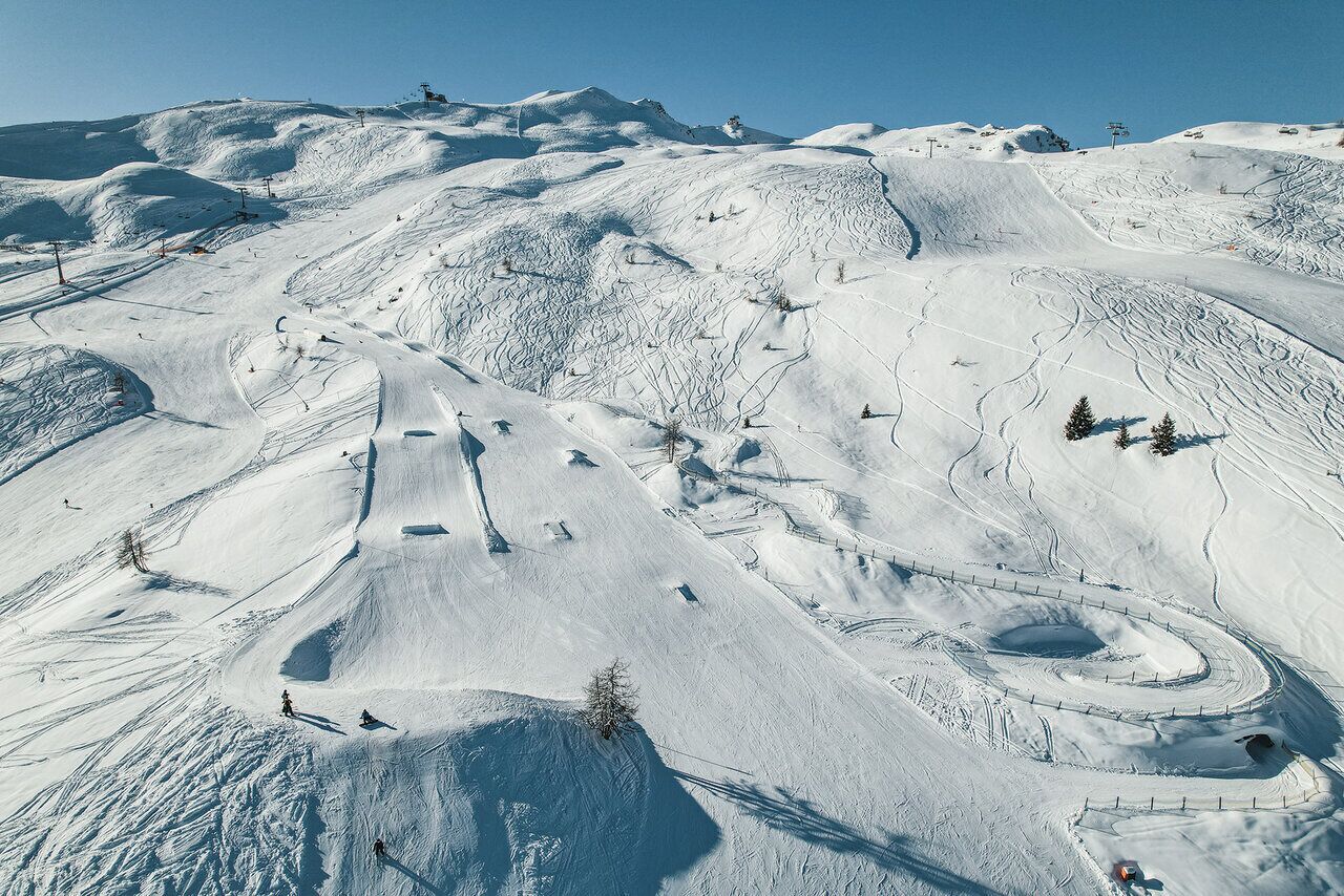 A snow-covered ski slope with ski lifts, trees, and a clear sky.