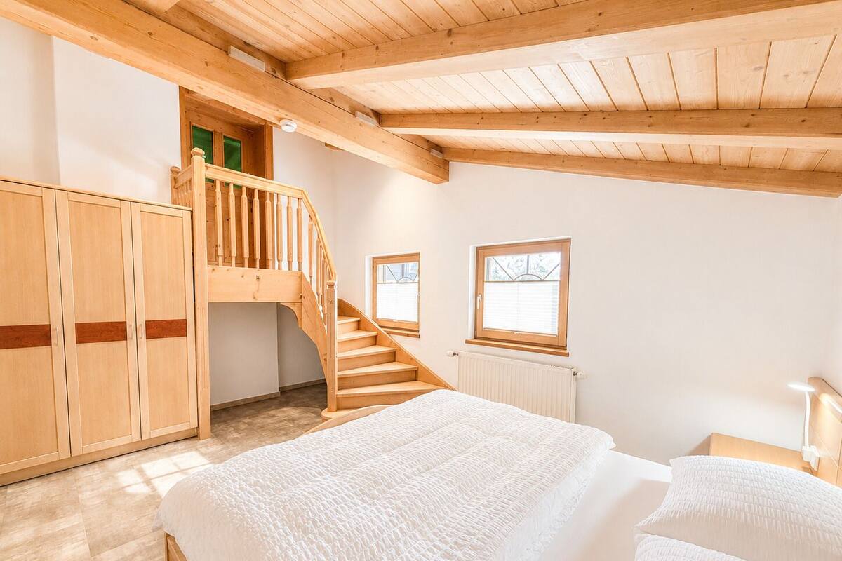 A bedroom with a wooden staircase, a bed, and a window.