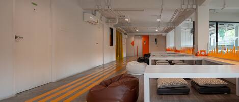 A modern office space with a long corridor, white walls, and a bright orange stripe on the floor. There are bean bags, a white table, and a sofa.