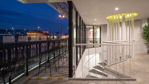 A modern hotel interior with a glass railing overlooking a cityscape, a staircase with a unique lighting feature, and a bar area with seating. - Yaks House Hostel (Bangkok)