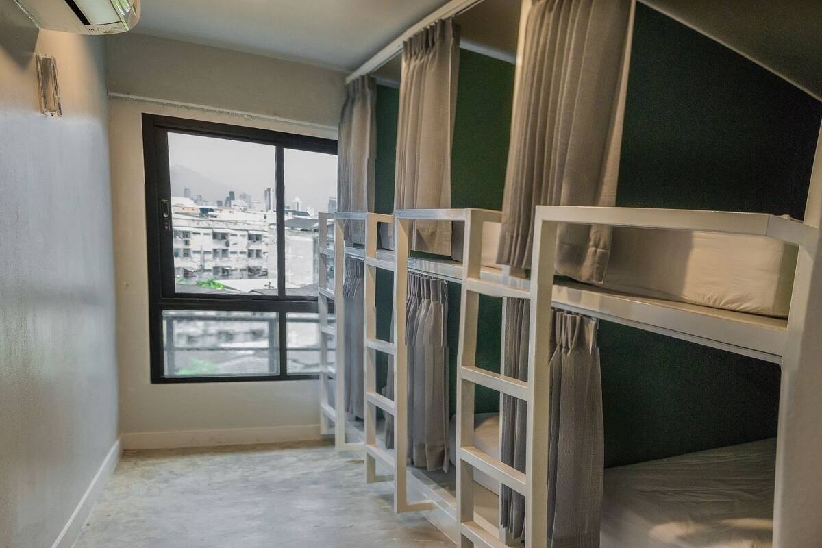 A room with bunk beds, a large window with a city view, and a white air conditioning unit on the wall.