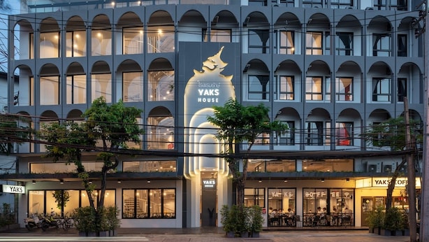 A modern building with a prominent 'YAKS HOUSE' sign, multiple balconies, and a ground-level coffee shop. - Yaks House Hostel (Bangkok)