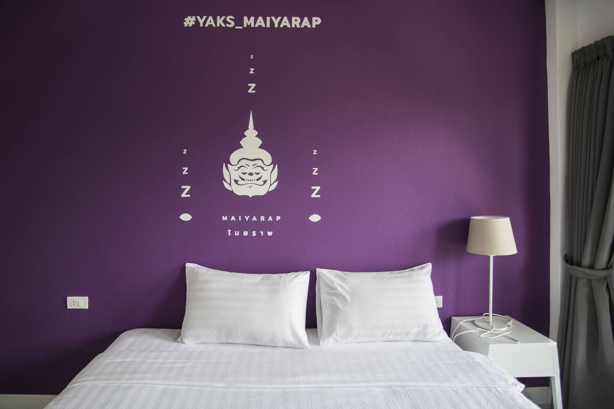 A hotel room with a purple wall, white bedding, and a bed with two pillows.