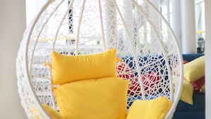 A white wicker hanging chair with yellow cushions in a bright, modern interior. - Yaks House Hostel (Bangkok)