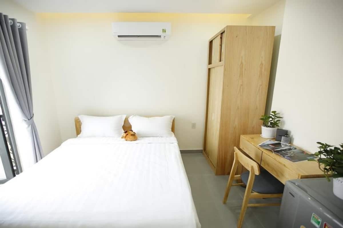 Ein Hotelzimmer mit einem Bett, einem Schreibtisch mit Stuhl, einem kleinen Tisch mit Pflanze und einer Klimaanlage.