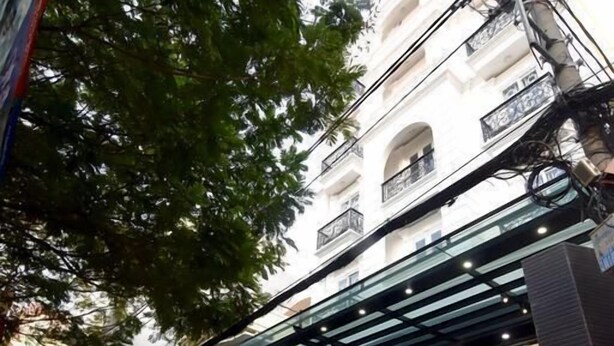 Entrada de un hotel con fachada de vidrio, un cartel que anuncia apartamentos con servicios y un área exterior techada.