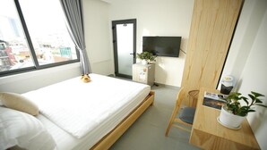 Una habitación de hotel con cama, escritorio, silla, televisor en la pared y ventana con cortinas.