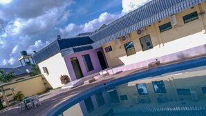 A swimming pool with a clear view of the surrounding buildings, including a house with a distinctive pink door and a blue roof. - The Prince Charles Hotel (Lusaka)