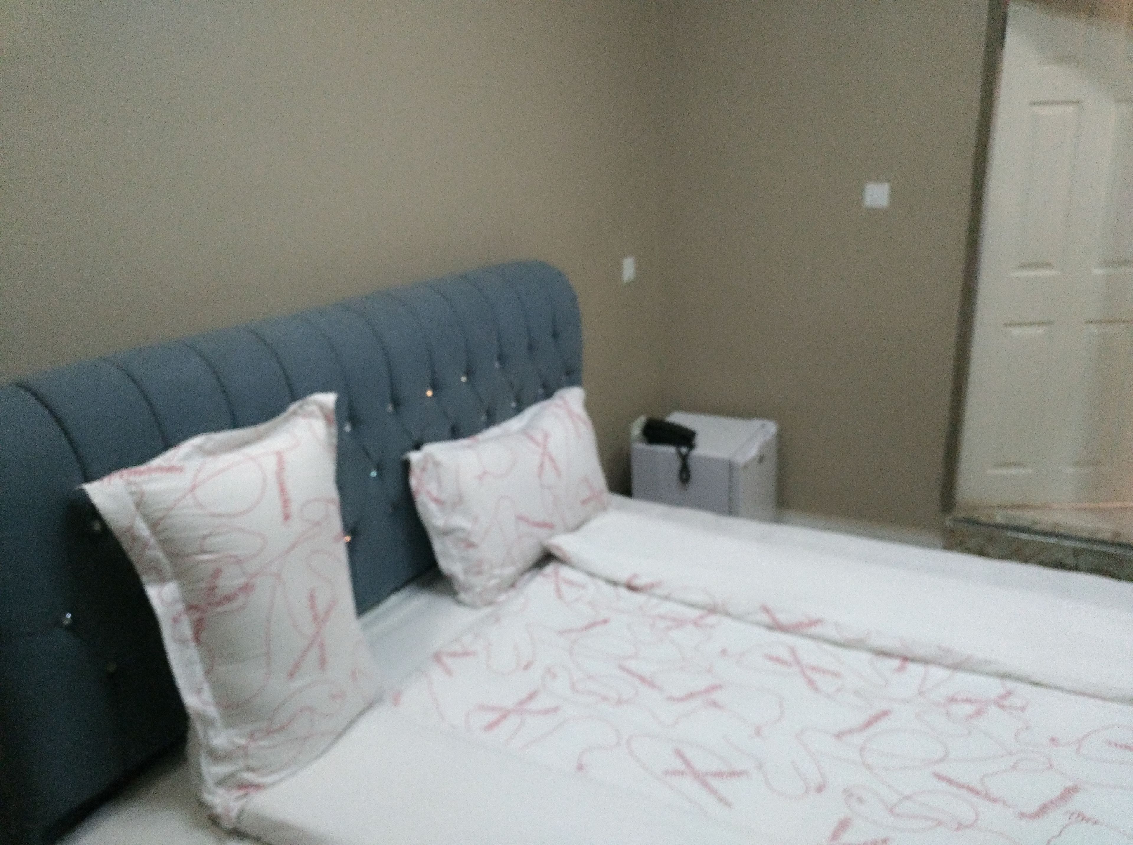 A bedroom with a blue headboard, two pillows, a bed with a patterned bedspread, a small bedside table, and a nightstand.