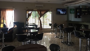 A hotel lobby with a bar area, a television displaying 'TITLE RIVALS', and a chandelier. - The Prince Charles Hotel (Lusaka)