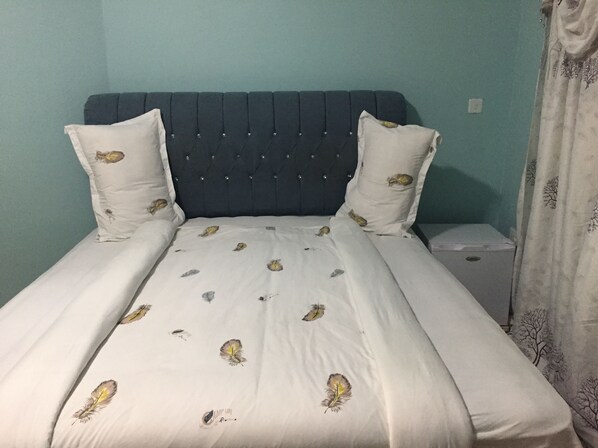 Una cama con edredón blanco con diseños de plumas, flanqueada por dos almohadas blancas con diseños similares.