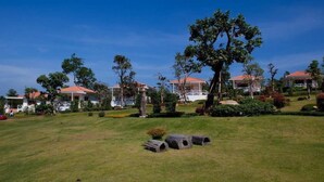 A grassy area with several buildings in the background, each with a red roof. There are trees and shrubs around the buildings. - Keawanongburi Resort (Nakhon Ratchasima)