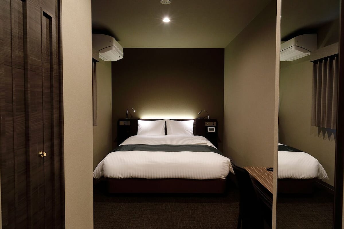 A hotel room with a bed, bedside lamps, a mirror, and a ceiling light.