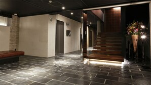 A modern lobby with a stone-tiled floor, a wooden bench, an elevator, and a staircase with a wooden railing. - Act Hotel Roppongi (Tokyo)