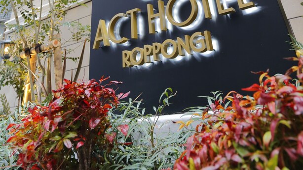 The exterior of the Act Hotel Ropongi with a prominent sign, red flags, and surrounding greenery. - Act Hotel Roppongi (Tokyo)