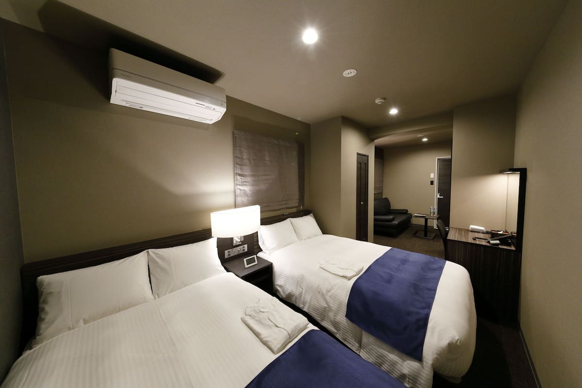 A hotel room with two beds, a desk, a chair, a mirror, and an air conditioning unit.