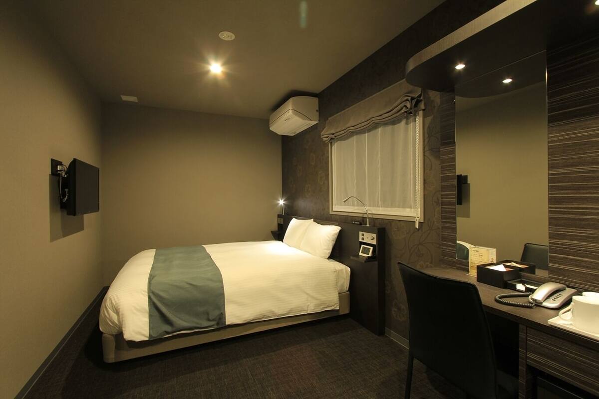 A hotel room with a bed, bedside table, desk, chair, and a mirror.