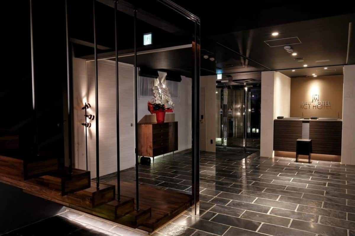 A modern hotel lobby with a reception desk, a staircase, and a glass partition.
