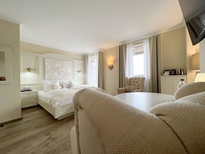 A hotel room with a large bed, a sitting area with a chair, a desk with a lamp, and a window with curtains.