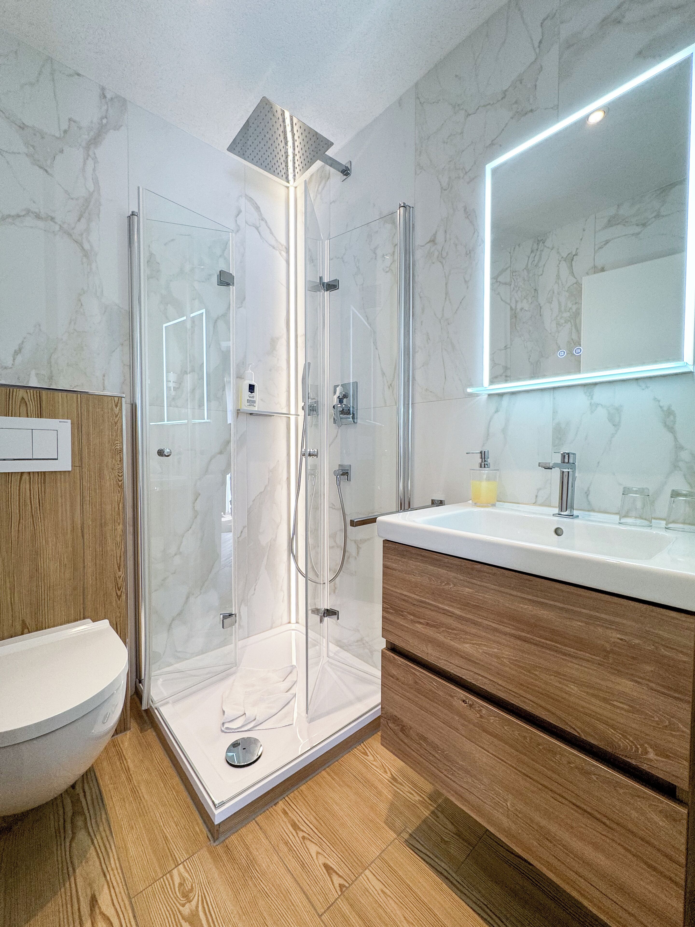 Ein modernes Badezimmer mit einer in Glas eingefassten Dusche, einem Holzwaschtisch und einer Marmor-Spritzschutzwand.
