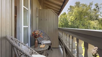 Ein Holzbalkon mit Korbstühlen und einem Tisch, eine Vase mit Blumen und Blick auf Bäume.