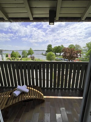 A balcony with a wooden bench and a towel, overlooking a lake with trees and boats. - Hotel Schlossblick Chiemsee (Prien am Chiemsee)