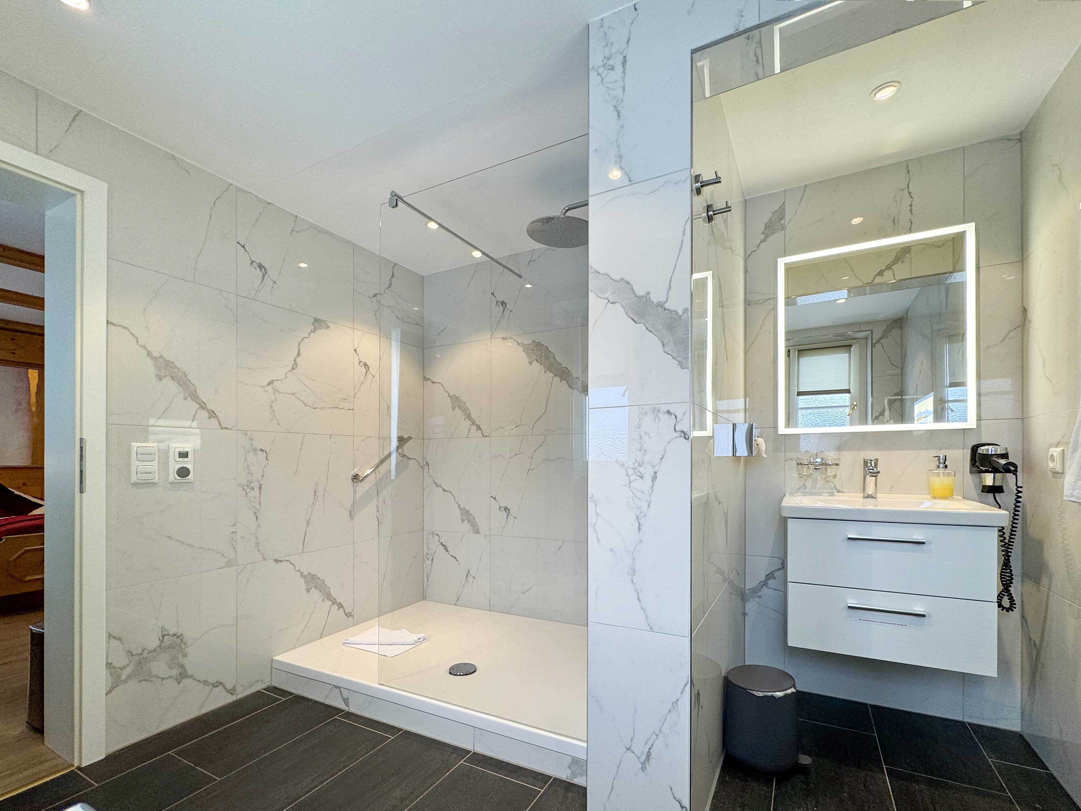 A modern bathroom with a glass-enclosed shower, a vanity with a mirror, and marble walls.